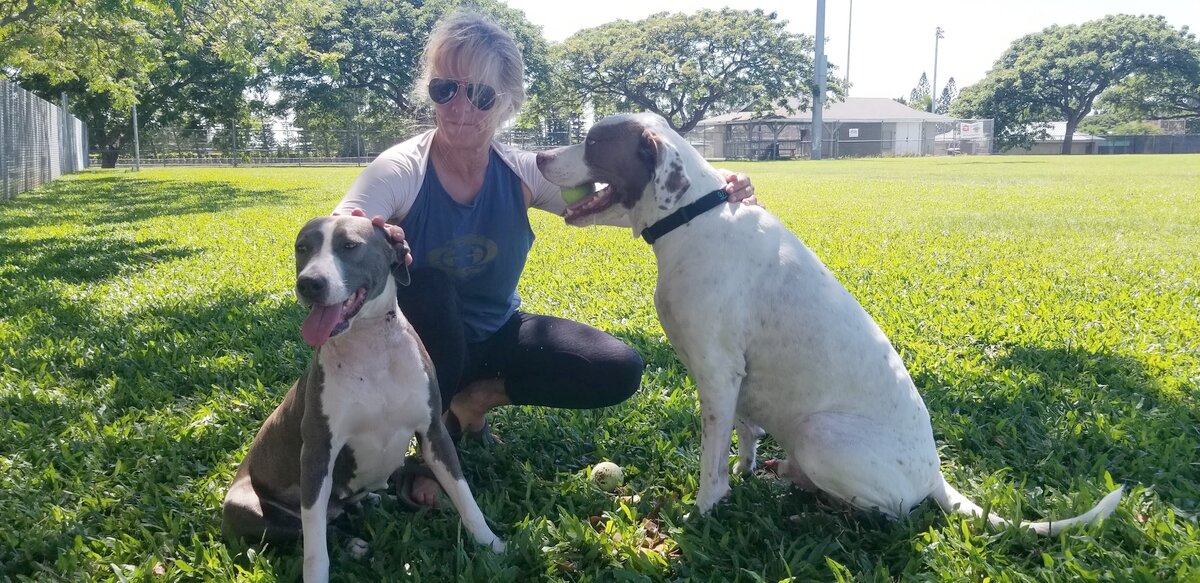 Lauren Turnbaugh Foo wearing sunglasses, kneeling in the grass with two dogs